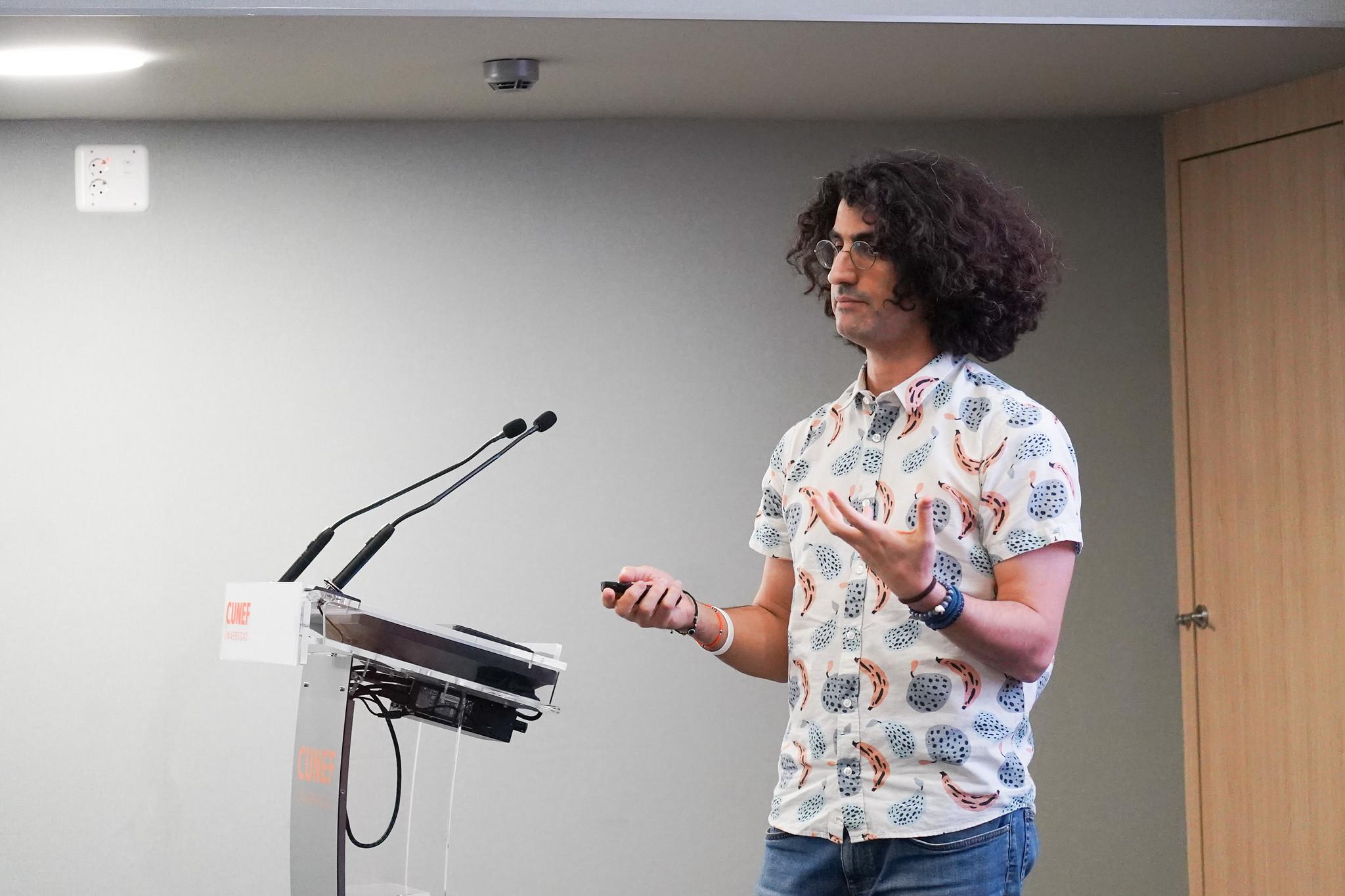 Un hombre con cabello rizado y una camisa de colores está presentando en un evento.