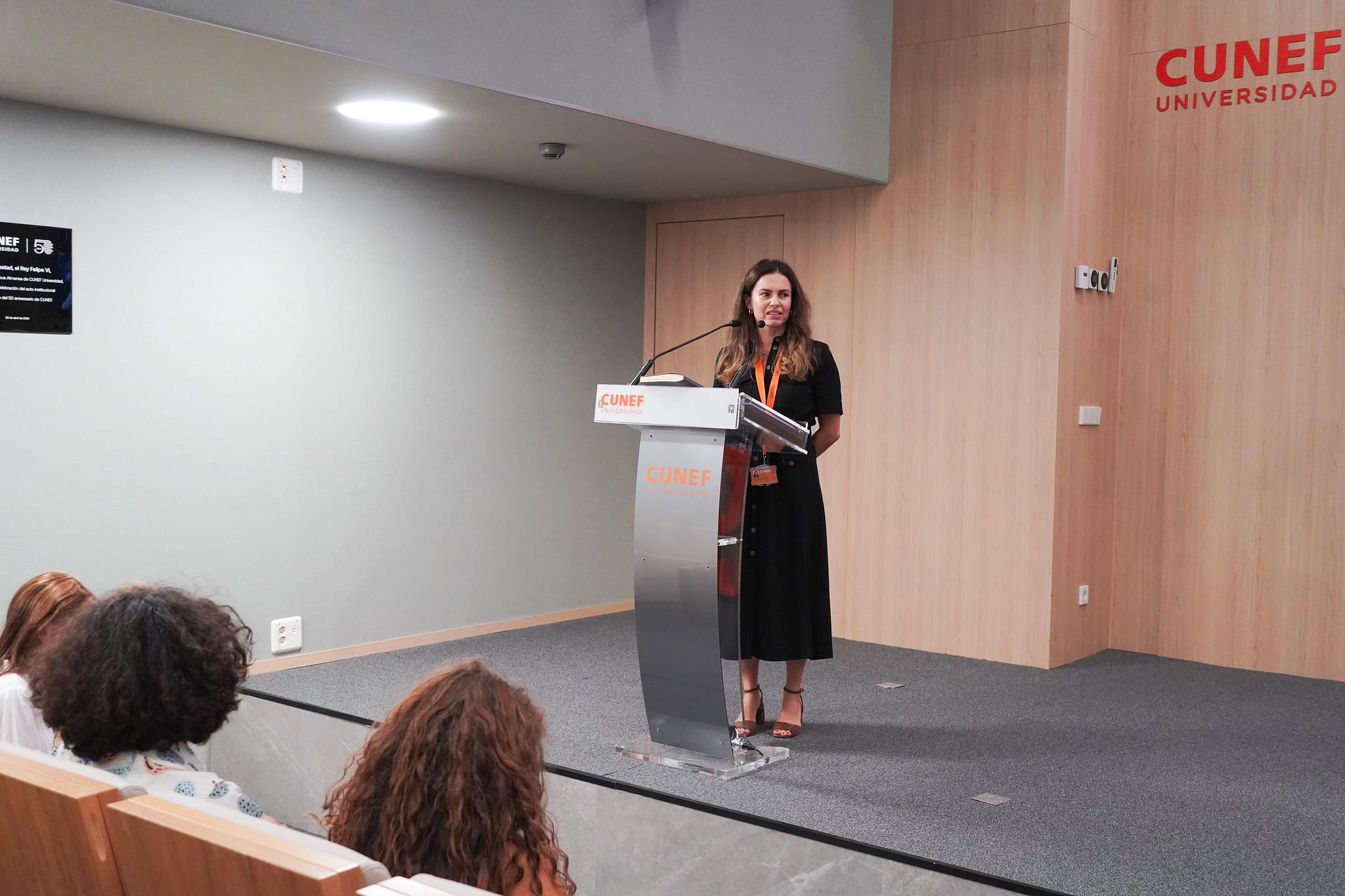 Una mujer de pie frente a un atril en un auditorio mientras habla a la audiencia.