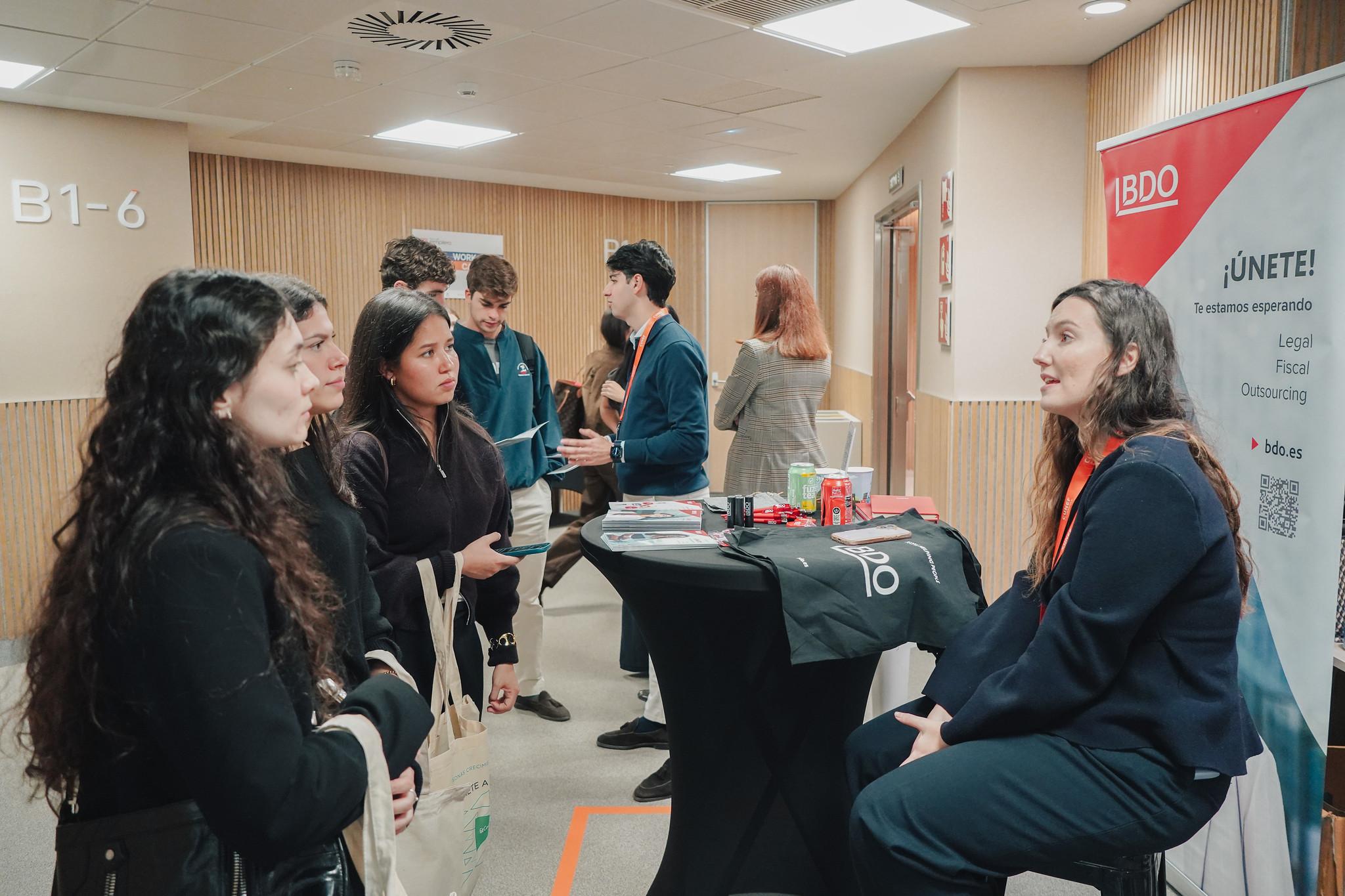 Un grupo de personas interactuando en un evento profesional frente a un stand de BDO.