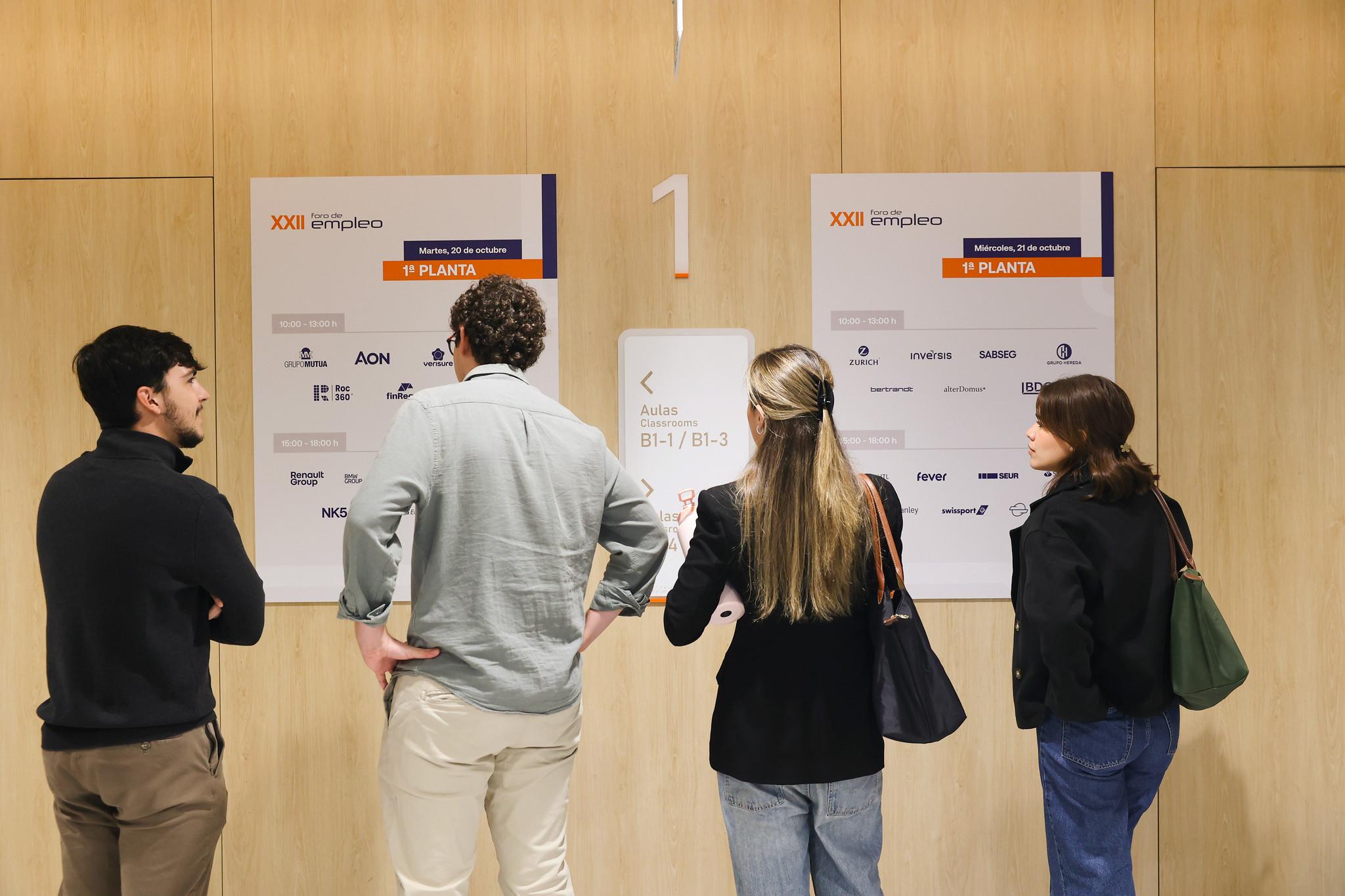 Un grupo de personas observa un panel informativo en la pared de un edificio.