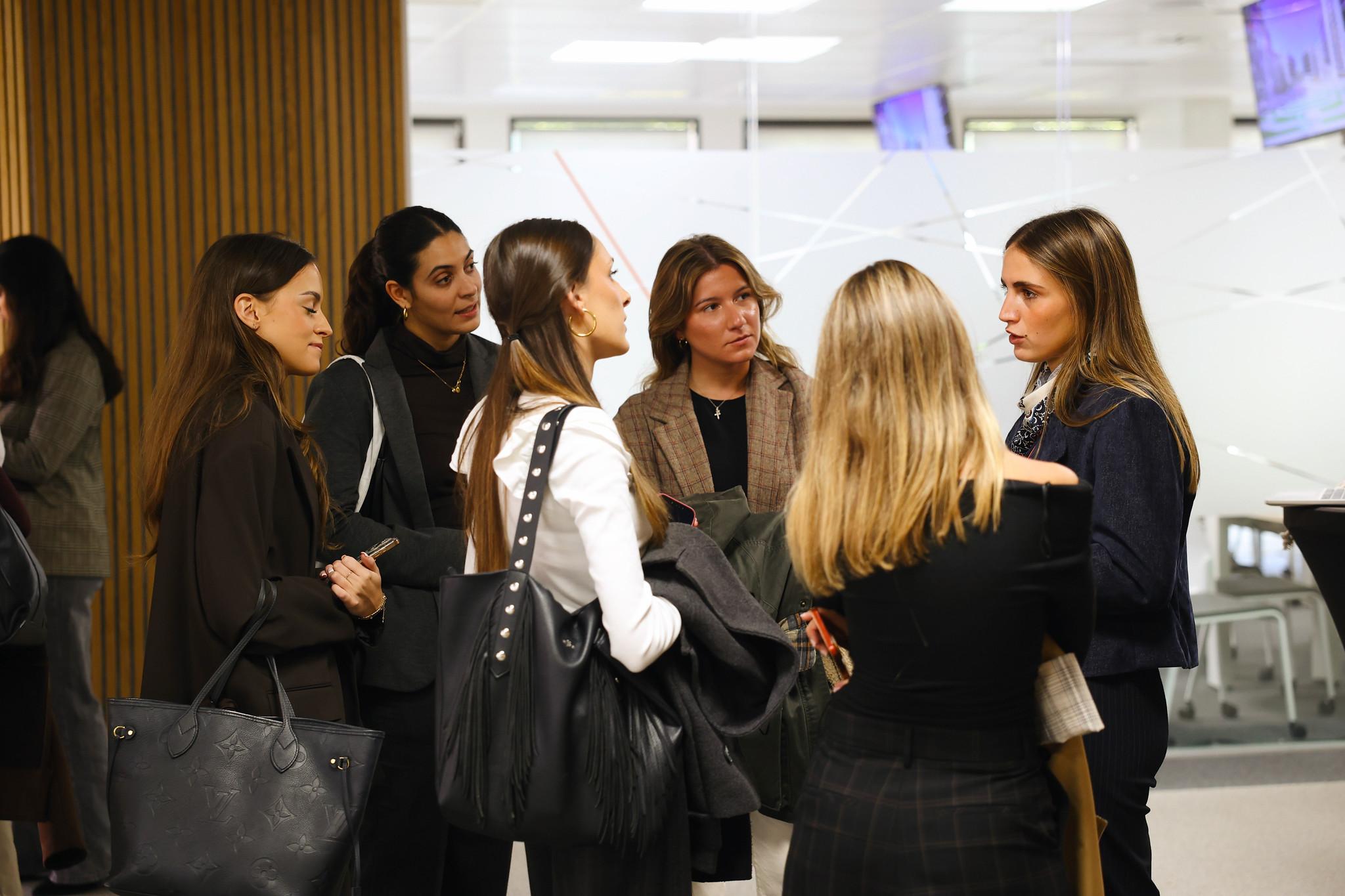 Un grupo de mujeres de pie conversando en un entorno profesional.