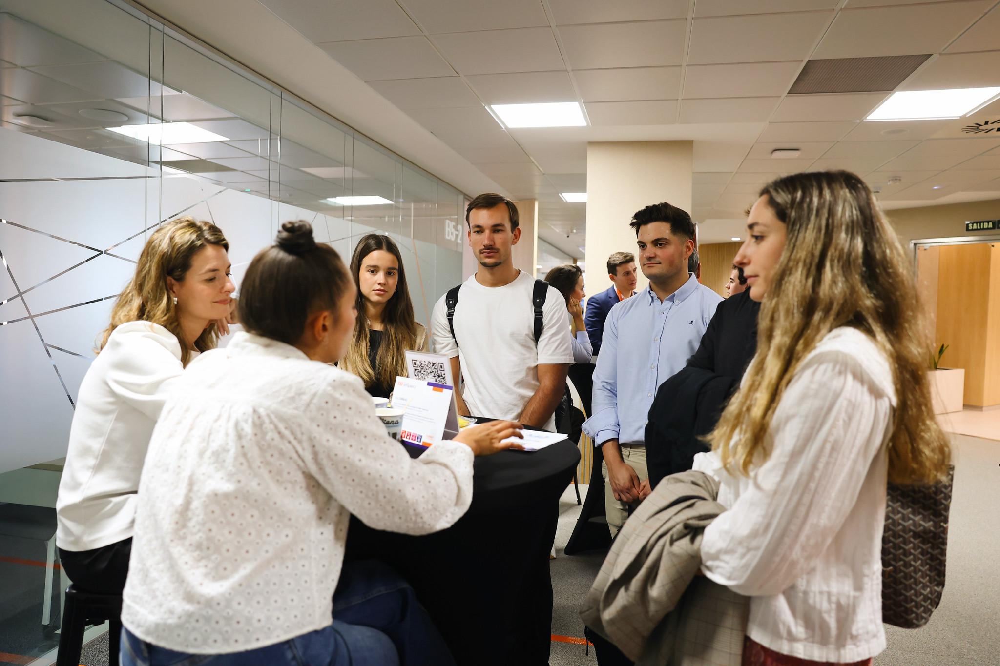 Un grupo de jóvenes interactúa en un evento de networking frente a una mesa.