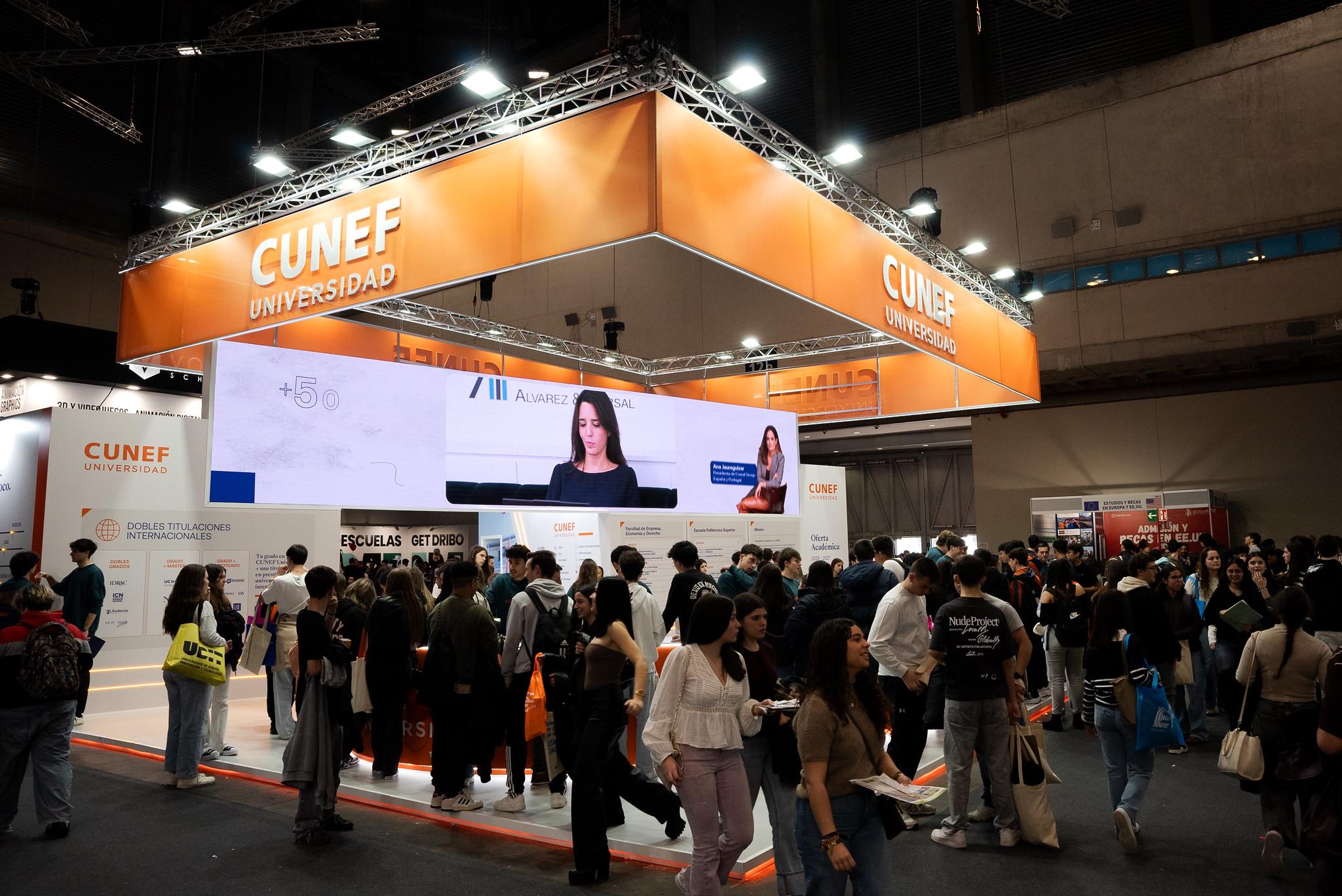 Una multitud de personas se agolpa frente a un stand de la Universidad CUNEF en un evento.