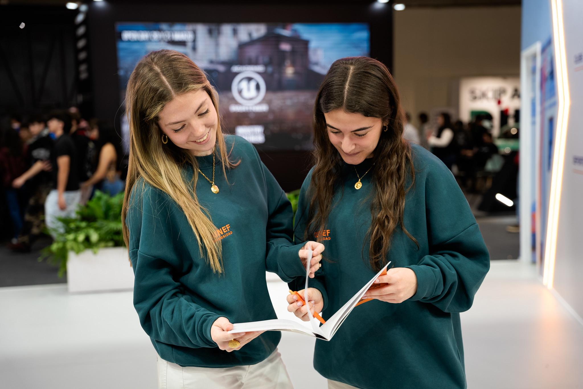 Dos chicas jóvenes revisando un libro en un evento.