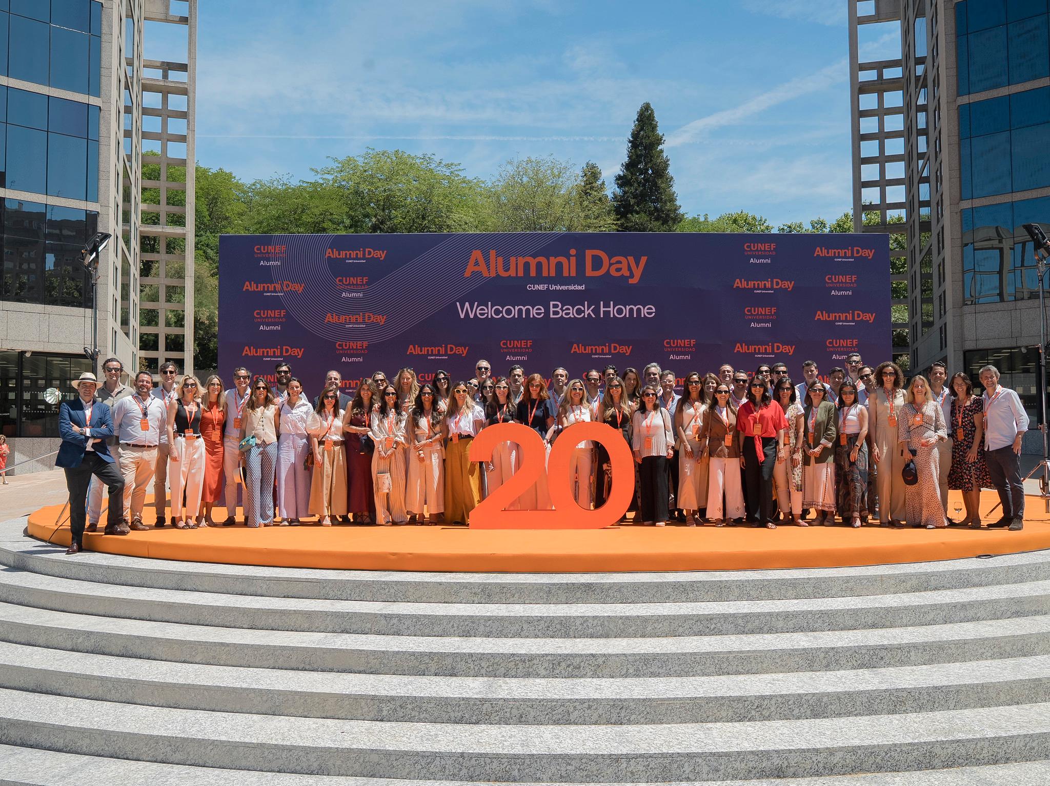 Grupo de personas reunidas en un evento de Alumni Day, celebrando el regreso a casa con un gran número 20 en el centro.