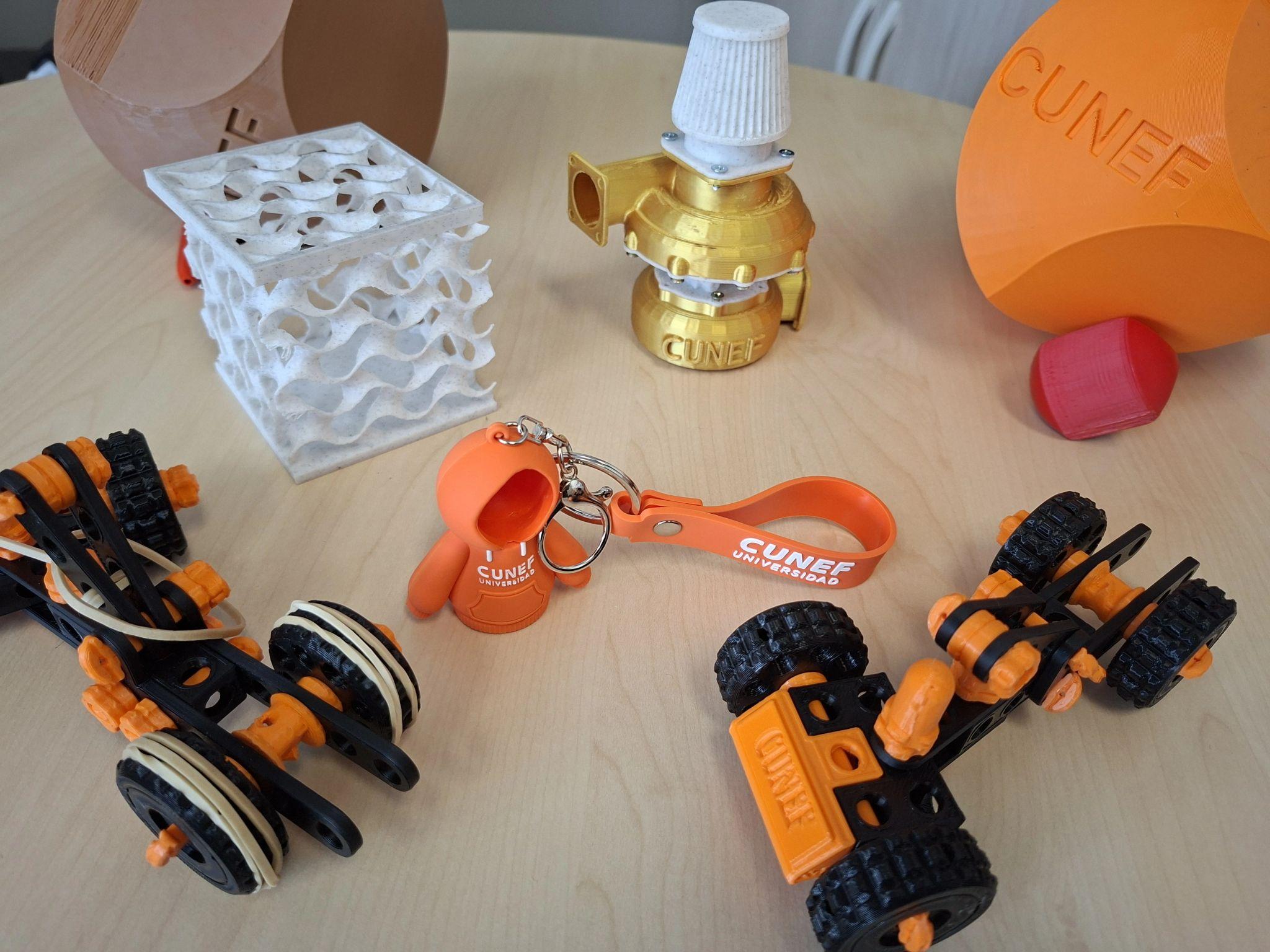 La imagen muestra una variedad de objetos en una mesa, incluyendo modelos 3D y un llavero.