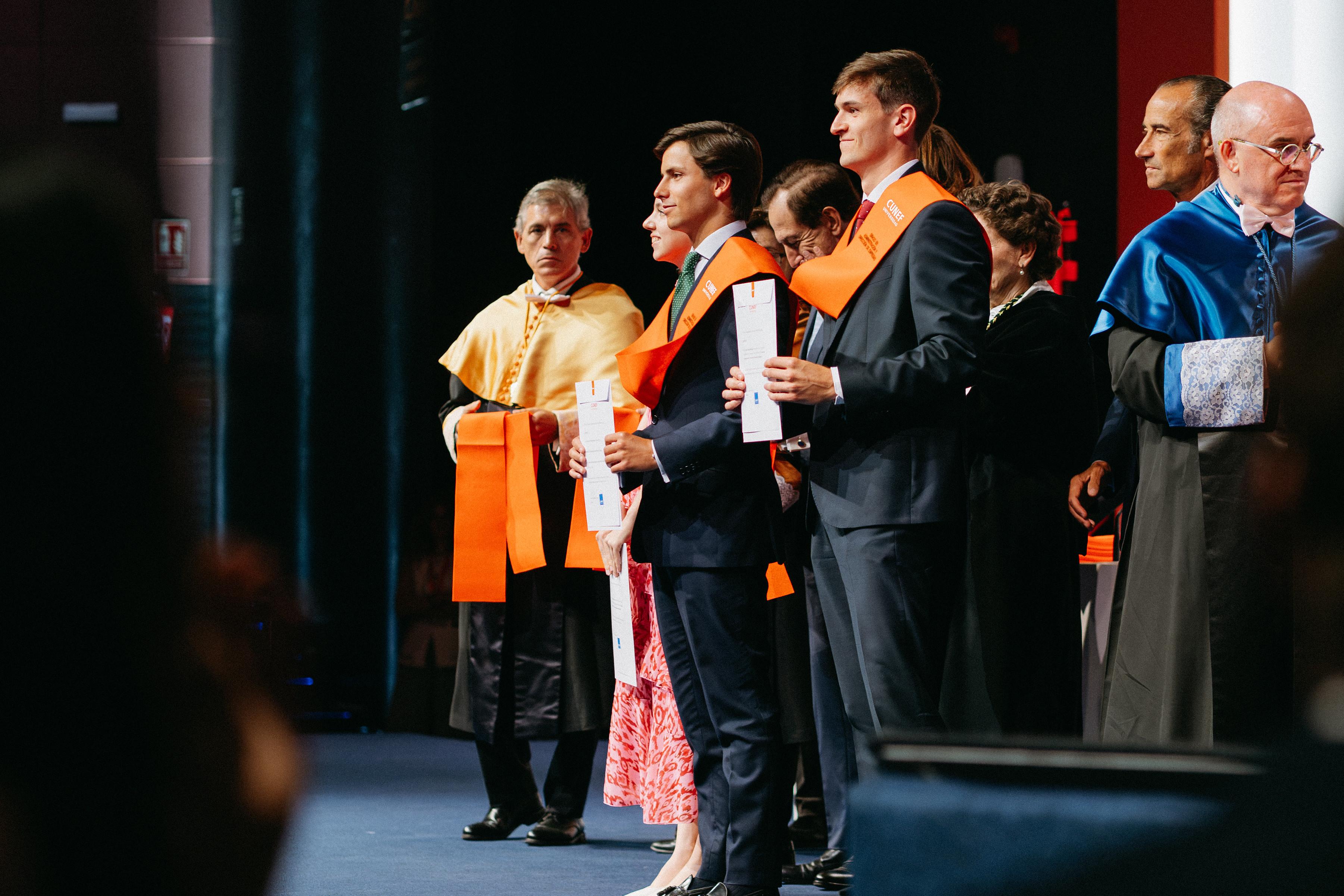 Una ceremonia de graduación con varios estudiantes que posan con sus diplomas y togas.
