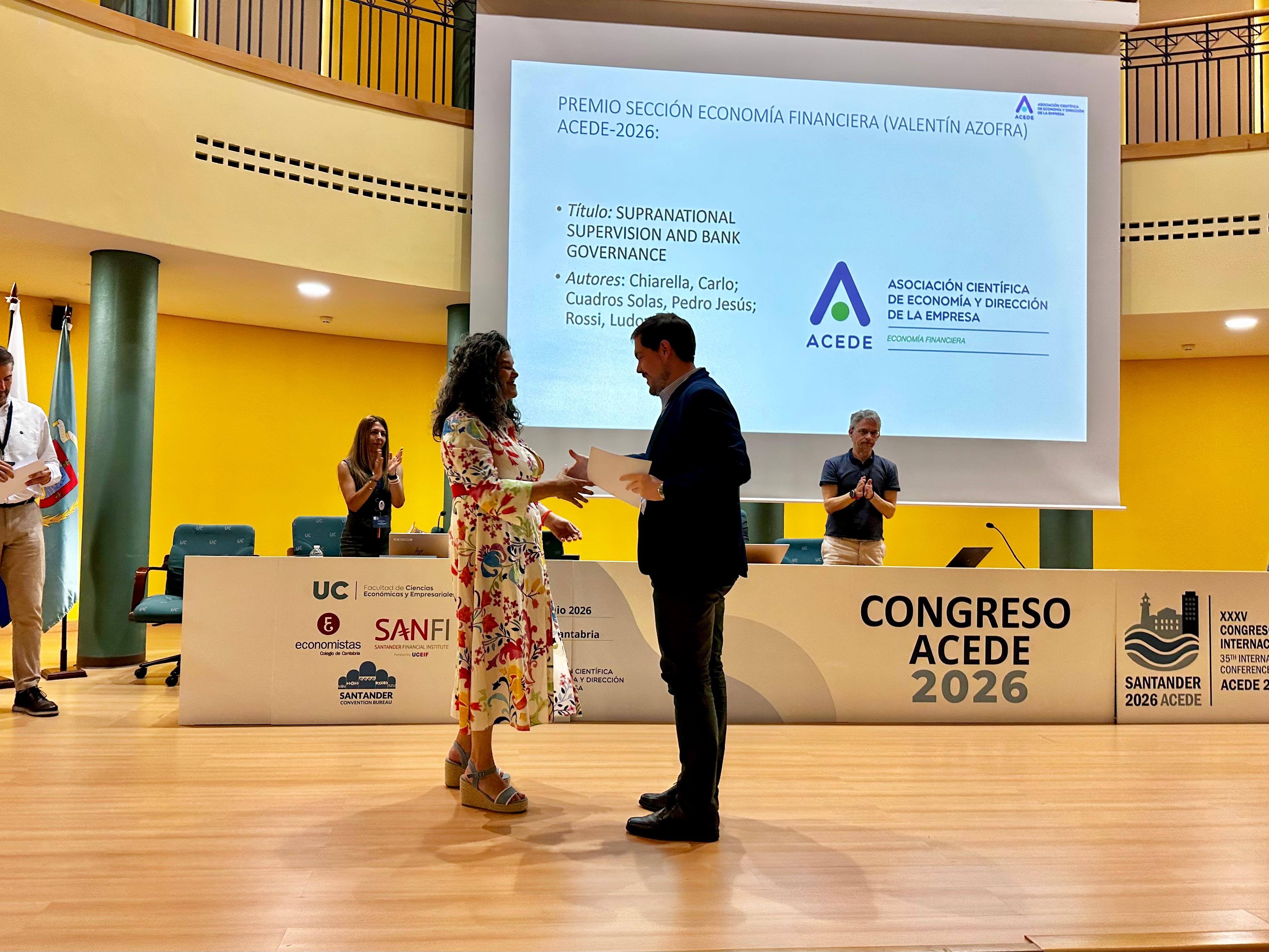 Una mujer entrega un premio a un hombre en un evento formal en un auditorio.