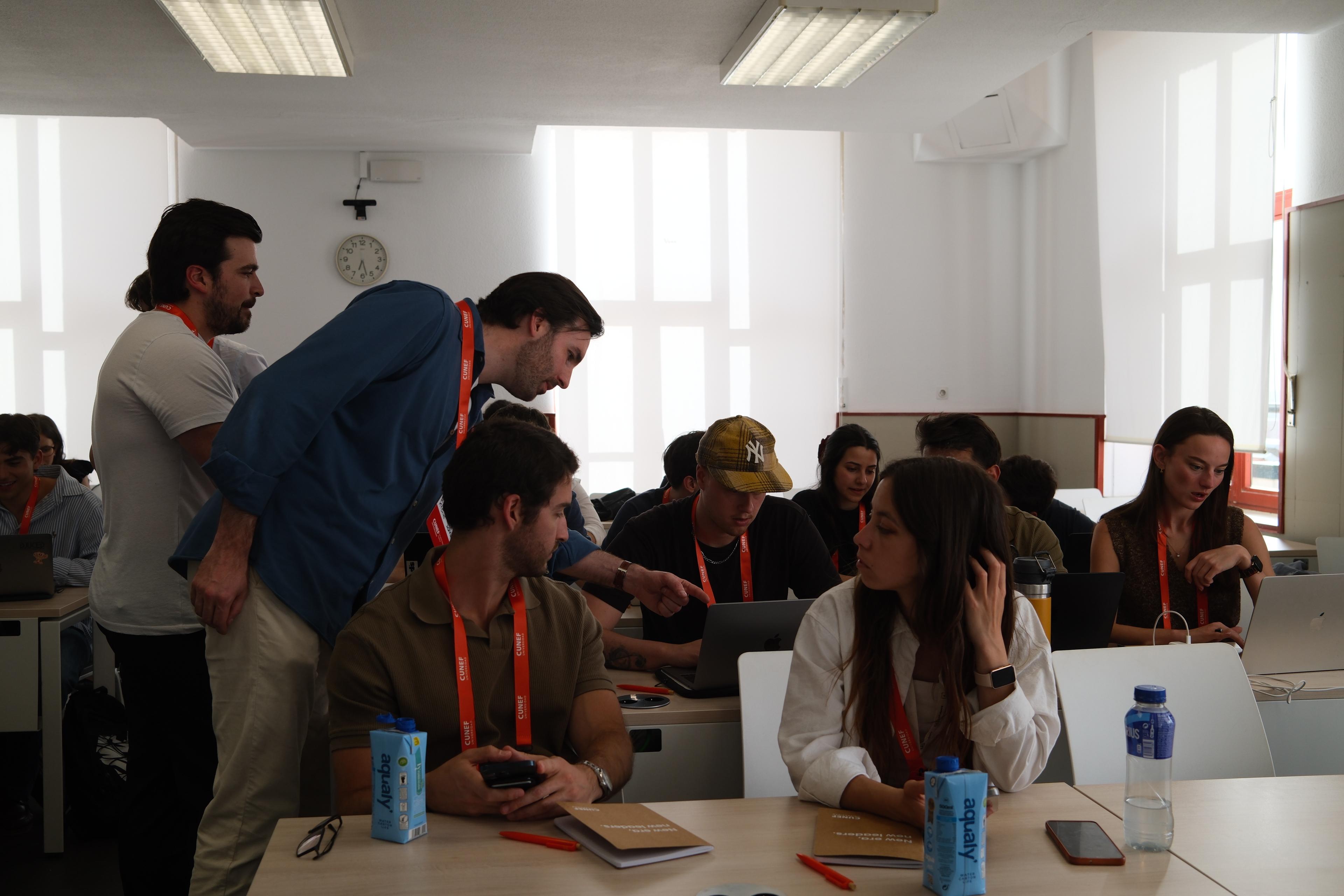 Un grupo de jóvenes interactúa en un aula mientras trabajan en sus computadoras portátiles.