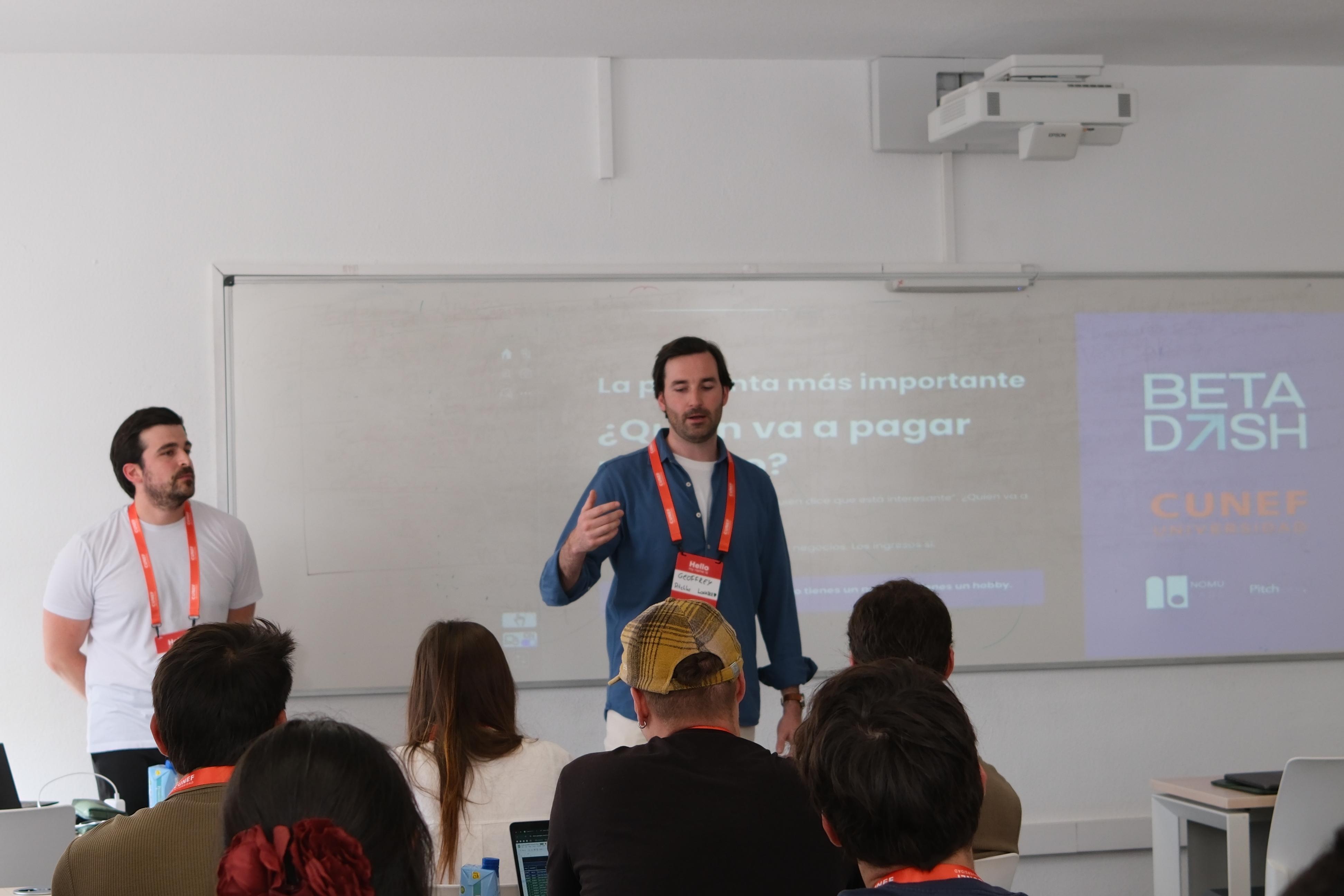 Una presentación en un aula, donde dos hombres hablan frente a un público interesado.