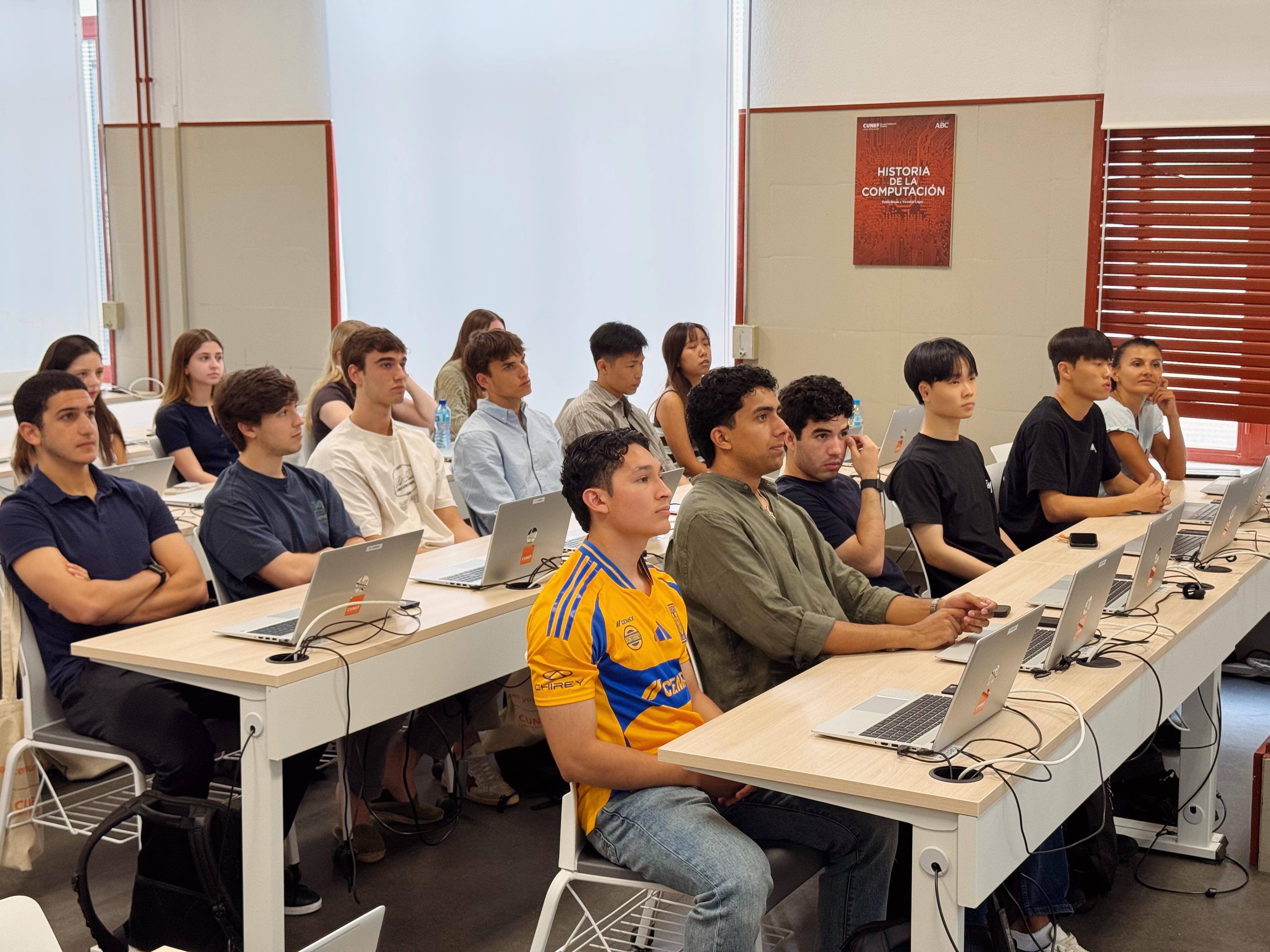 Un grupo de estudiantes sentados en un aula, frente a computadoras portátiles.
