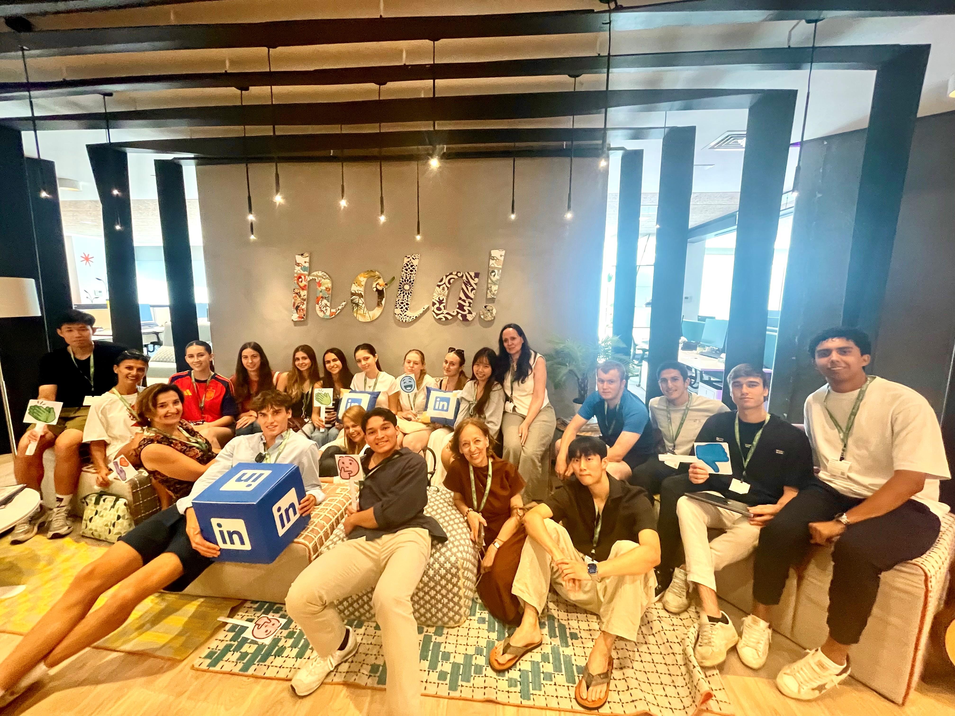 Un grupo de jóvenes posando en un espacio abierto, sosteniendo tarjetas y un cubo de LinkedIn.