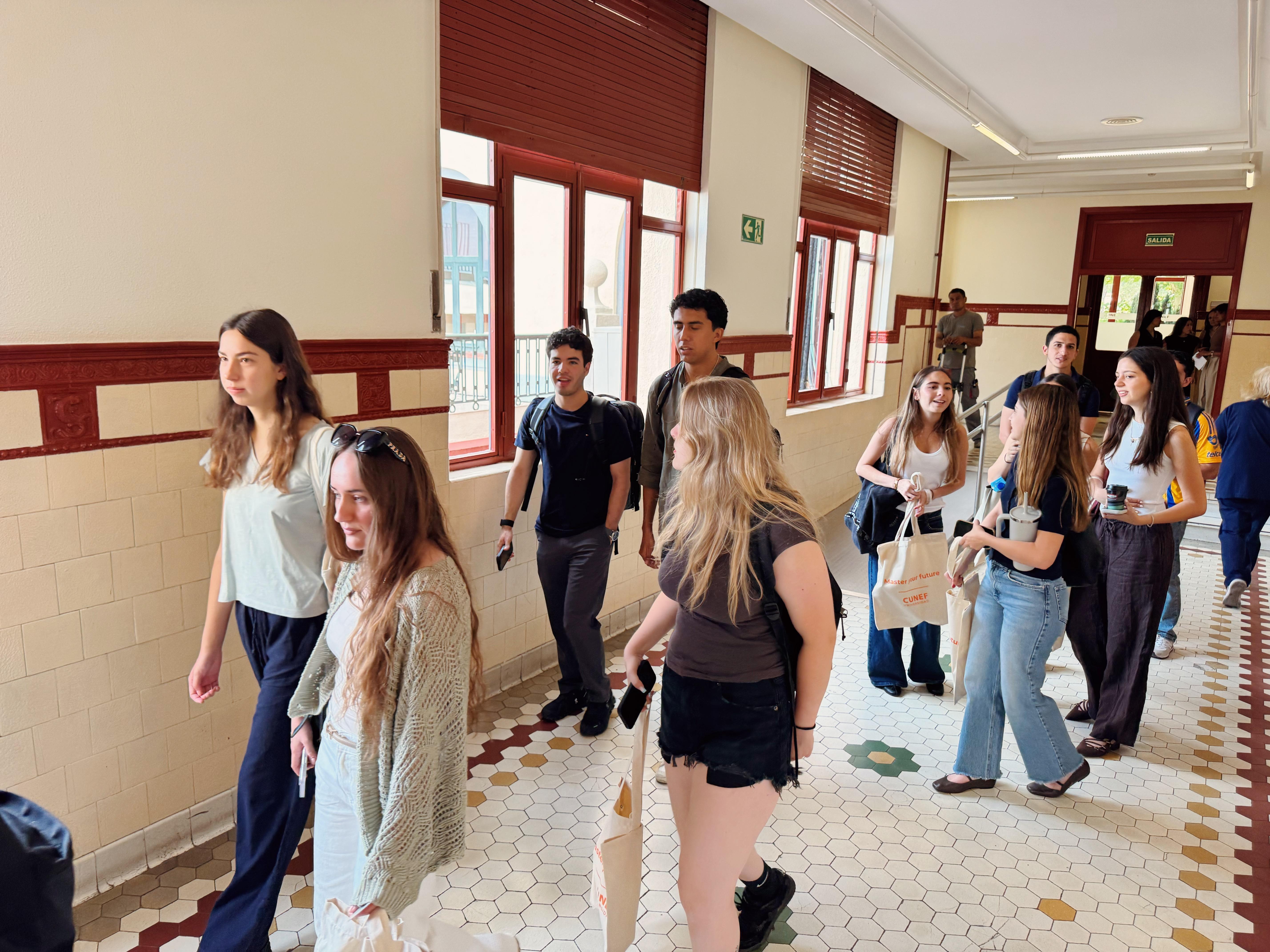 Un grupo de jóvenes camina por un pasillo iluminado con azulejos en el suelo.