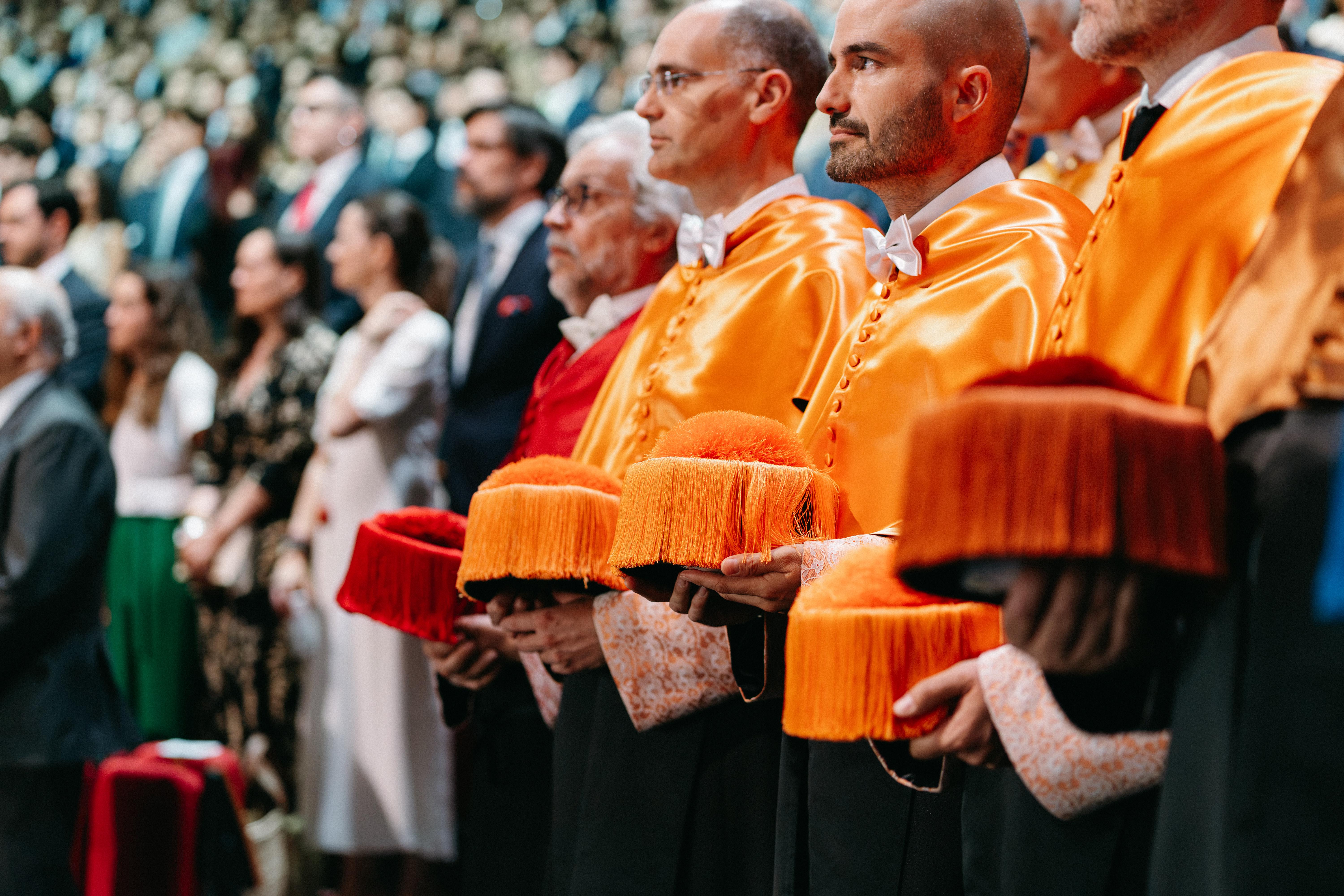 Un grupo de personas con trajes académicos y birretes en una ceremonia formal.