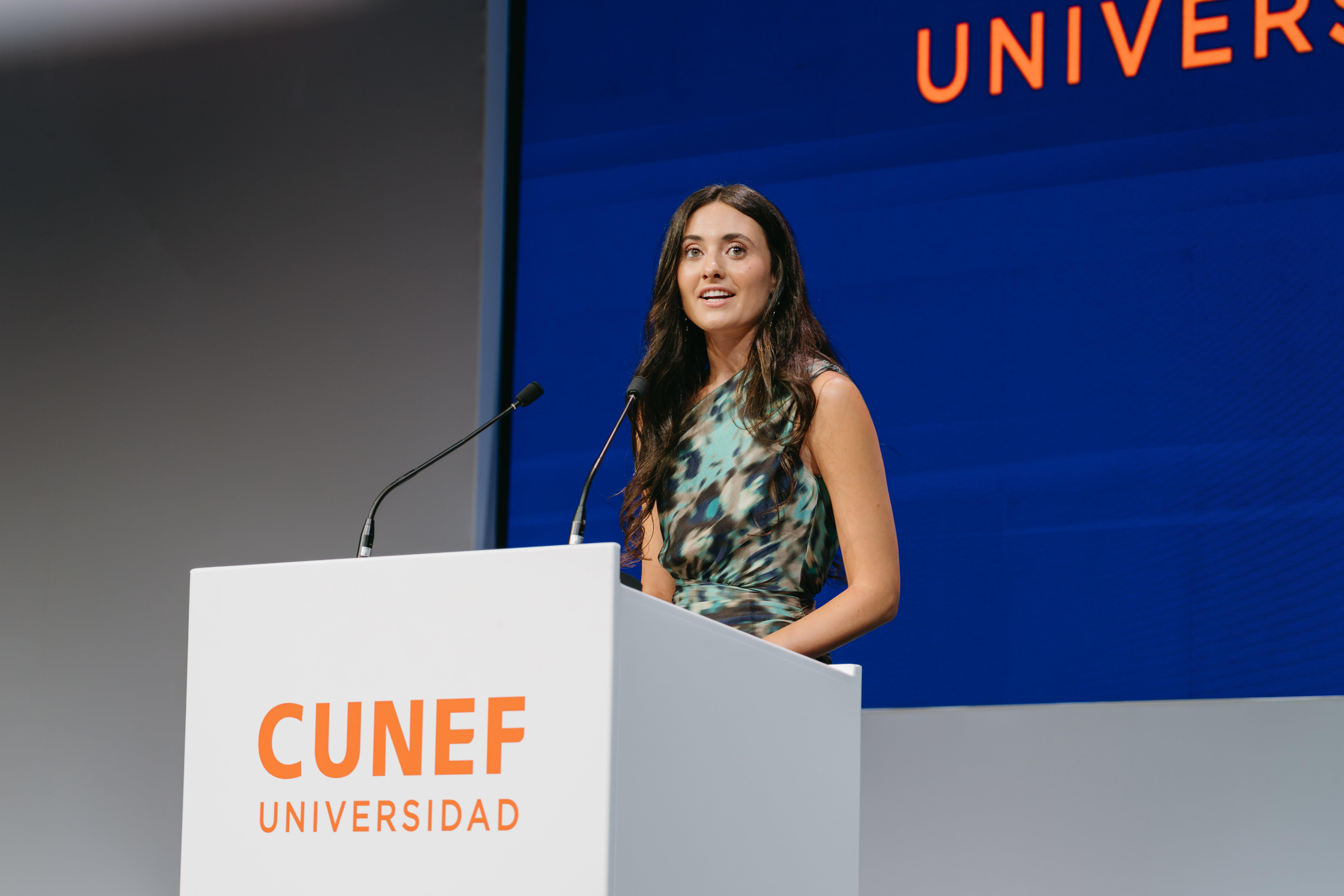 Una joven se encuentra en un podio hablando durante un evento universitario.