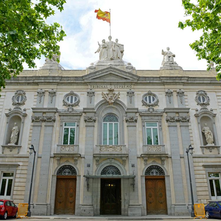 Edificio monumental con una fachada clásica y un mástil donde ondea la bandera de España.