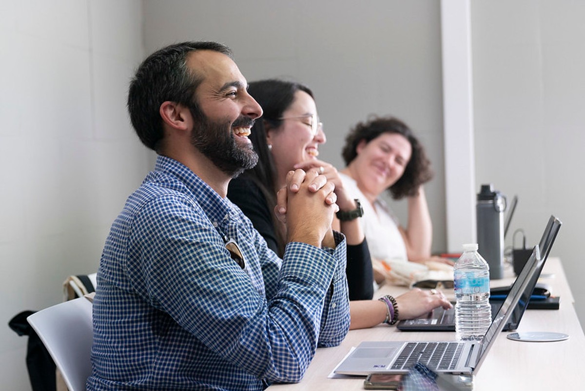 Un grupo de personas sonríe y se muestra alegre mientras trabaja en sus computadoras portátiles en una sala de reuniones.