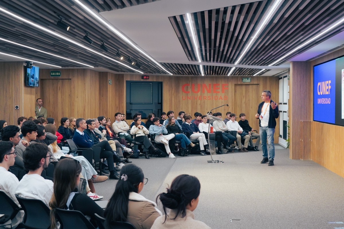 Una conferencia en un auditorio moderno con un ponente que habla frente a una audiencia numerosa.