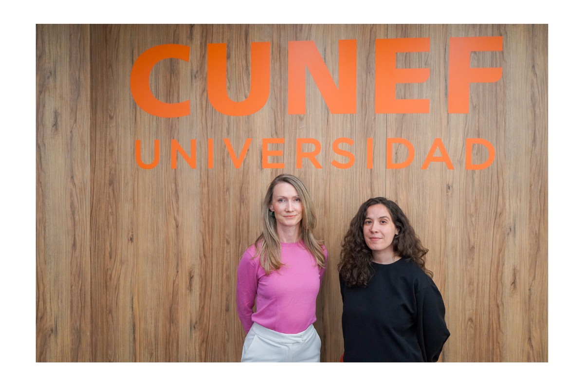 Dos mujeres posan frente a un fondo con el logo de CUNEF Universidad.