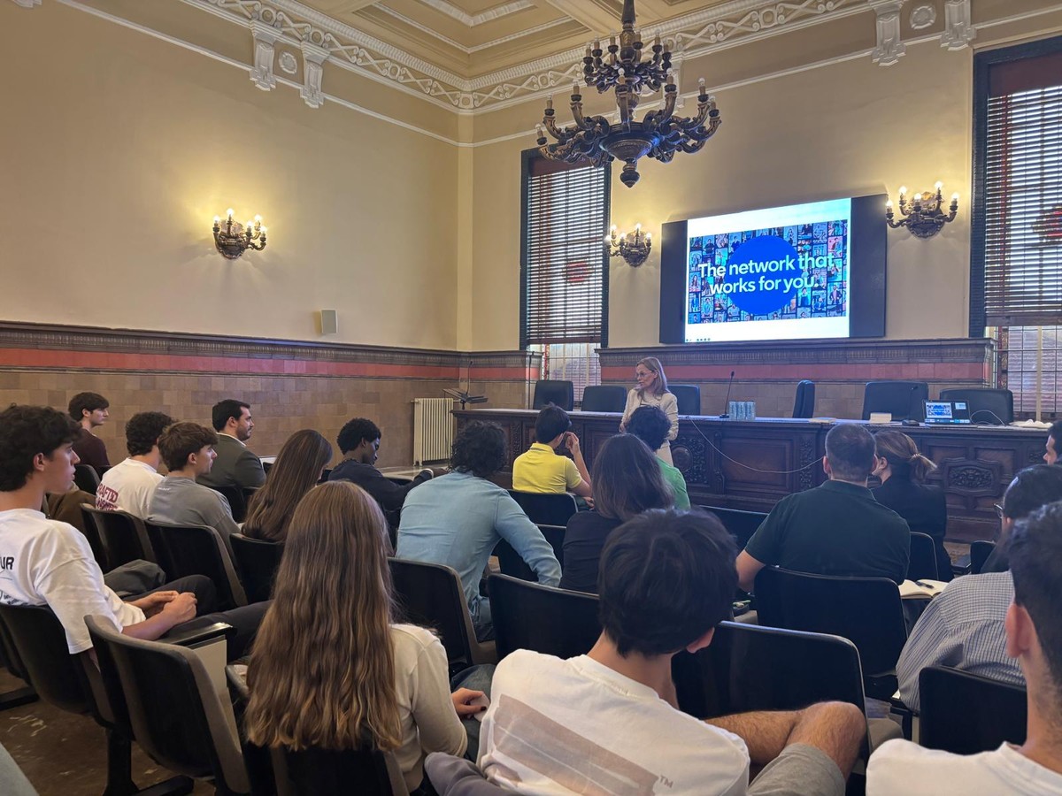 Una presentación en un salón con un grupo de estudiantes escuchando a una oradora frente a una pantalla.