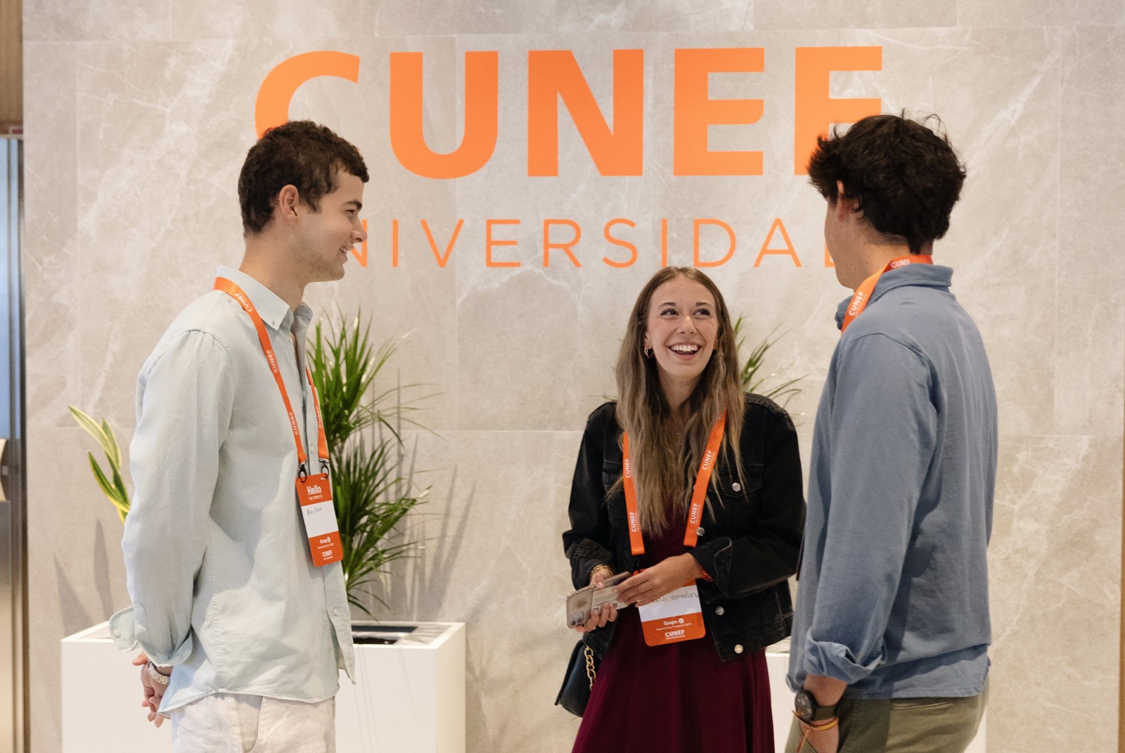 Tres estudiantes conversan y sonríen frente a un cartel de la universidad CUNEF.