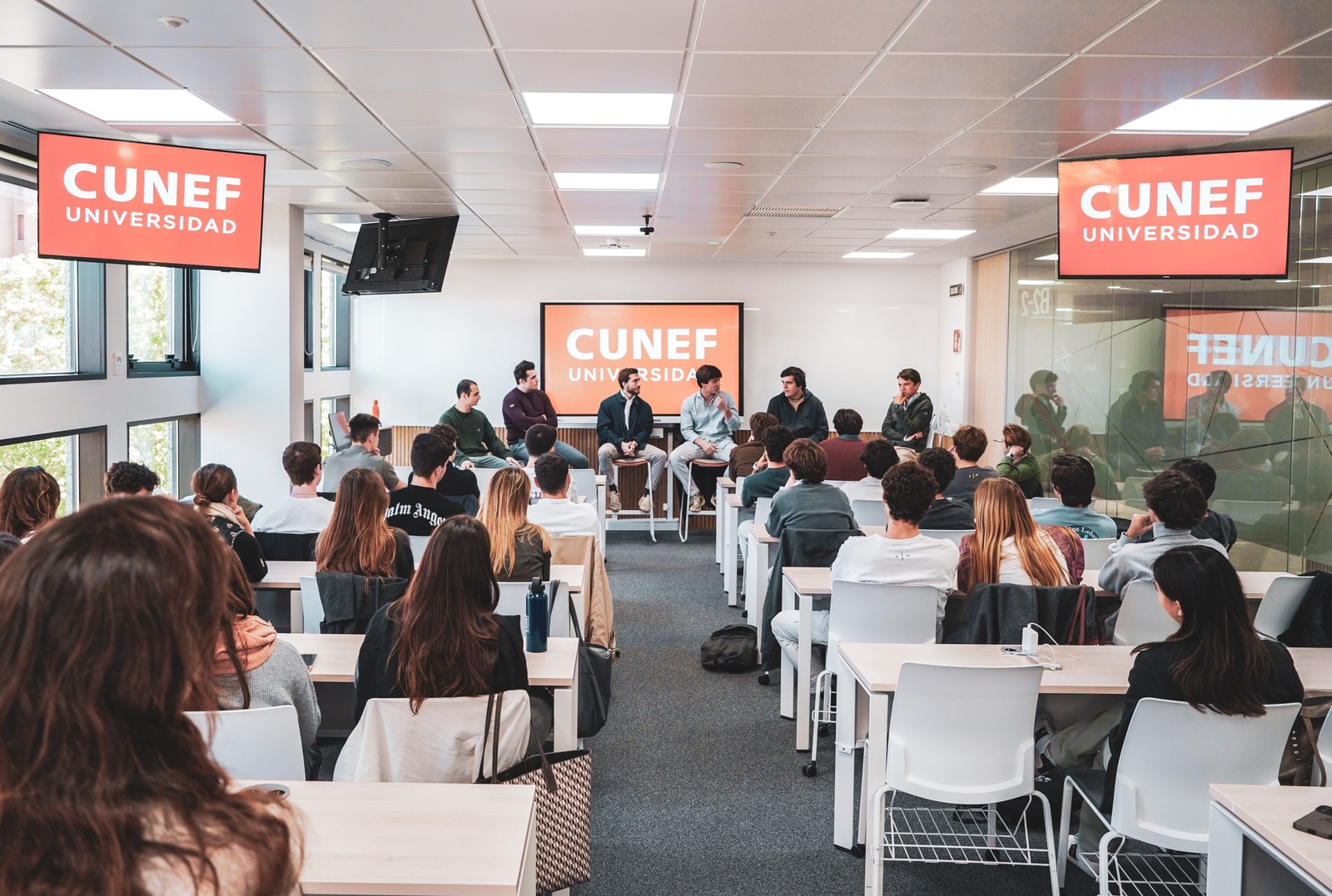 Un panel de discusión en un aula de la Universidad CUNEF con estudiantes presentes.
