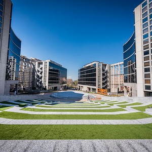 Una vista de un espacio urbano moderno con edificios de cristal y un área verde en el centro.
