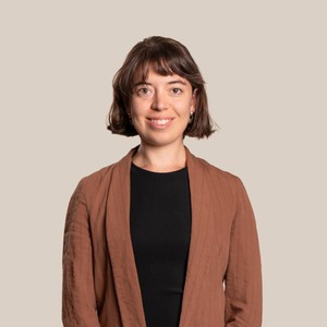 Una mujer sonriente lleva un traje de color marrón claro en un fondo beige.