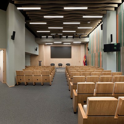 Una sala de conferencias moderna con asientos de madera y una pantalla al fondo.