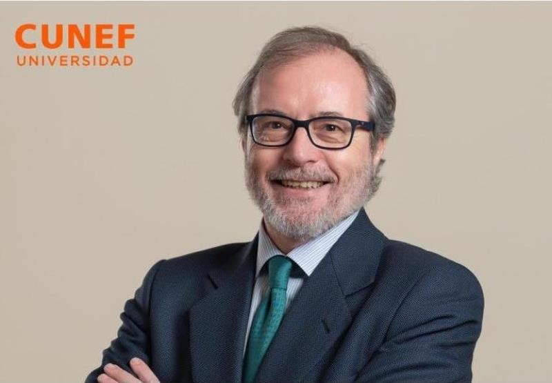 Retrato de un hombre con gafas y una sonrisa amable, vestido con un traje oscuro y una corbata verde.